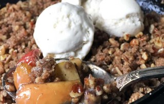 a spoonful of apple crisp coming out of a cast iron pan with melted ice cream