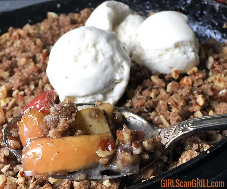 a spoonful of apple crisp coming out of a cast iron pan with melted ice cream