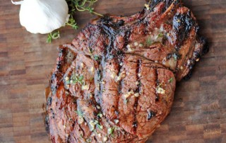 grilled ribeye on a wooden board with garlic nearby