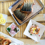 grilled fish on pan with bagels, lemon, capers and onions.