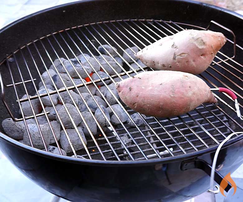 two sweet potatoes sitting on right side of grill with coals on left side