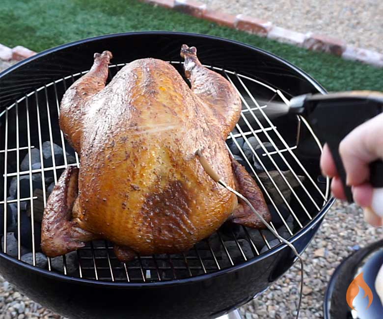 spraying smoked turkey on grill with liquid