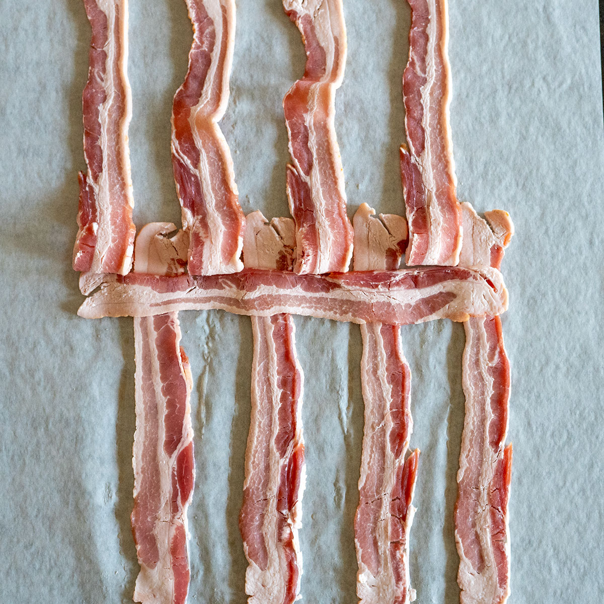 odd pieces of bacon folded back with one strip laying across strips that are down.