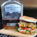 burger on a wood board next to bottle of whiskey