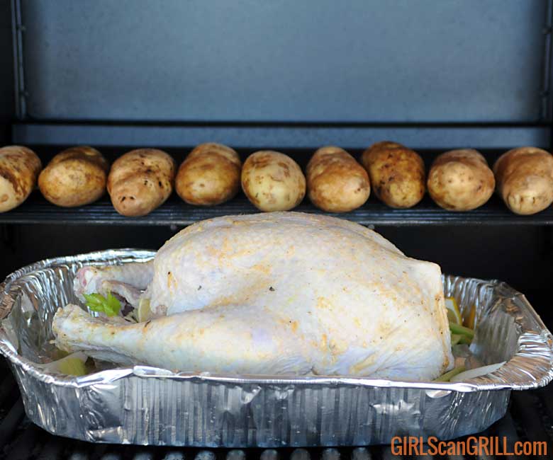 raw turkey in pan on grill with potatoes on warming rack