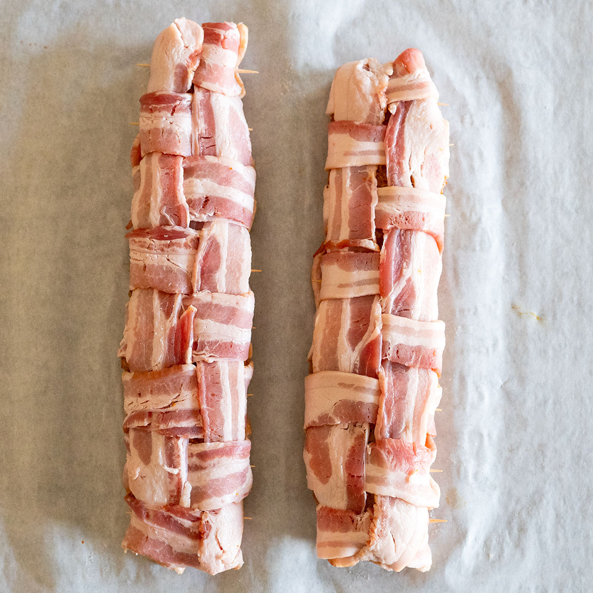 two bacon-wrapped pork tenderloins on table.