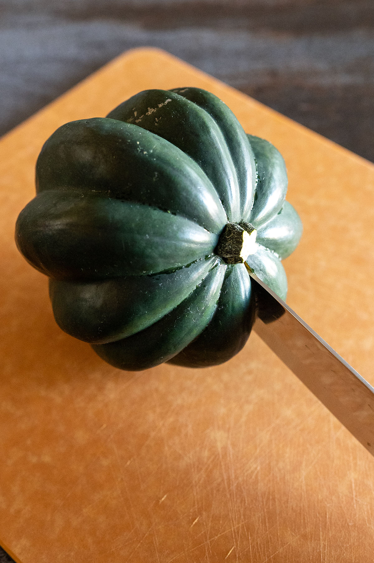 Knife cutting acorn squash under stem.