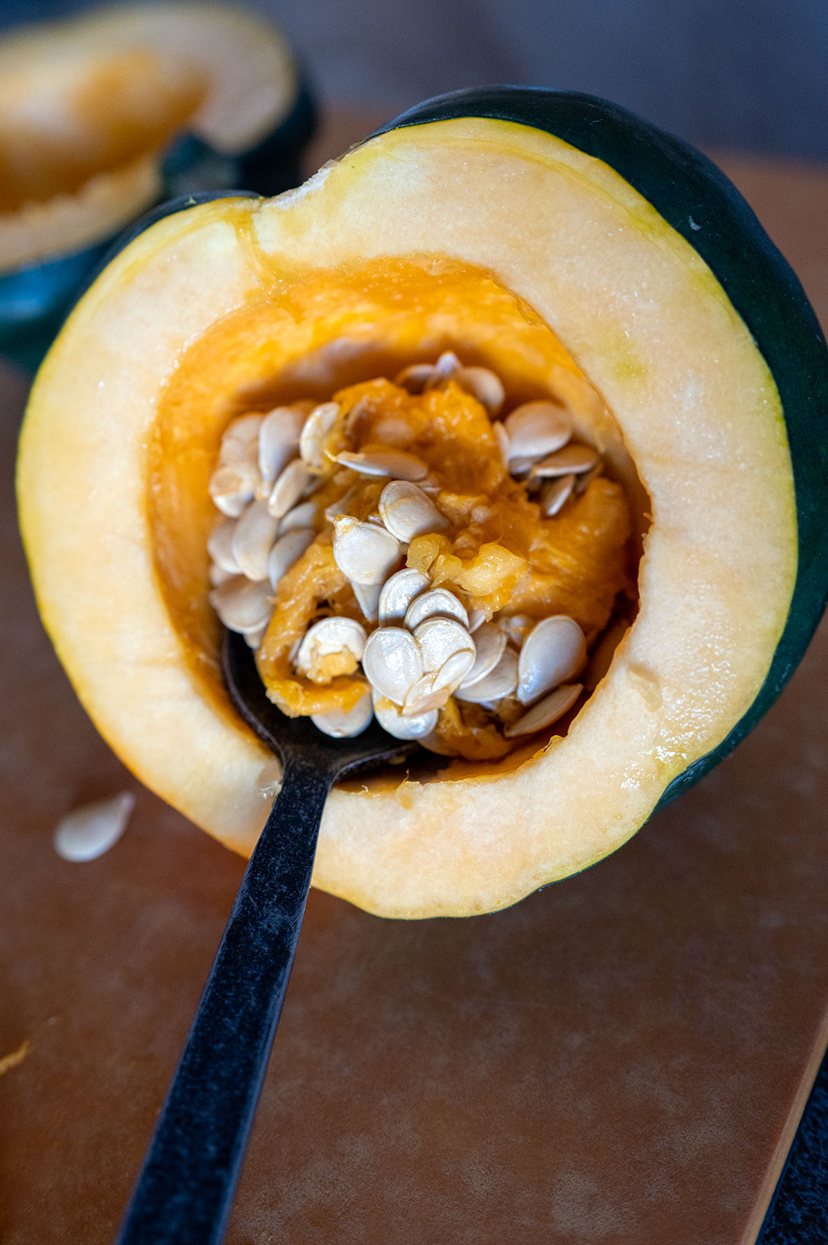 spoon scooping seeds from acorn squash half.