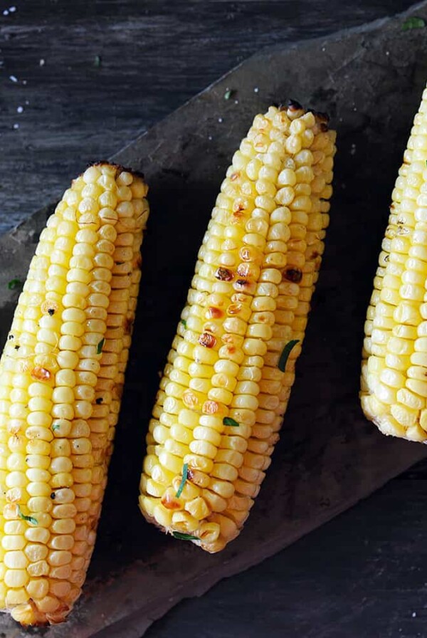 three ears of grilled corn on slate.