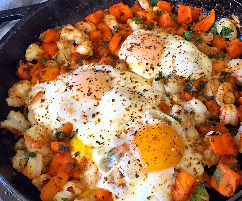 skillet with sweet potatoes and fried eggs