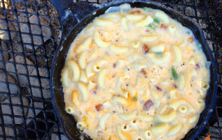 cast iron skillet of macaroni and cheese over a campfire
