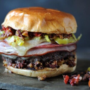burger stacked with ham and olive spread with gray background