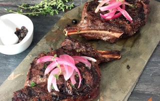 two elk chops topped with pickled red onions on a slate tile