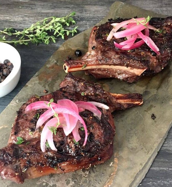 two elk chops topped with pickled red onions on a slate tile