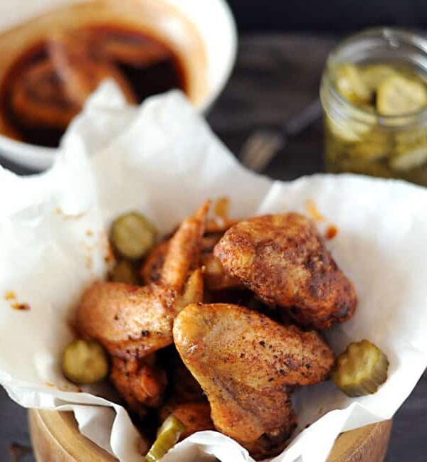 bowl of nashville hot chicken with sauce and pickles on side