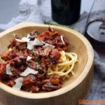 red meat sauce on top of bucatini pasta in wooden bowl