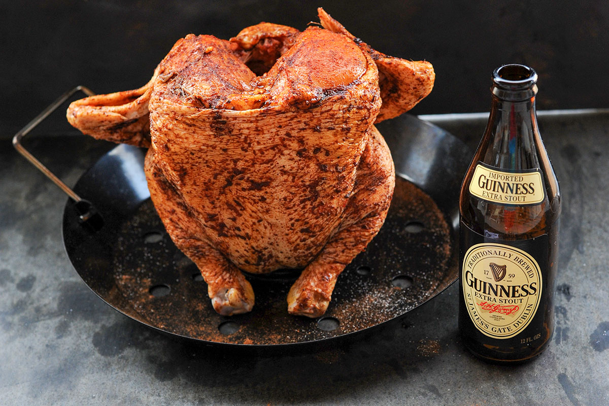Seasoned chicken on beer can roaster next to bottle of Guinness.