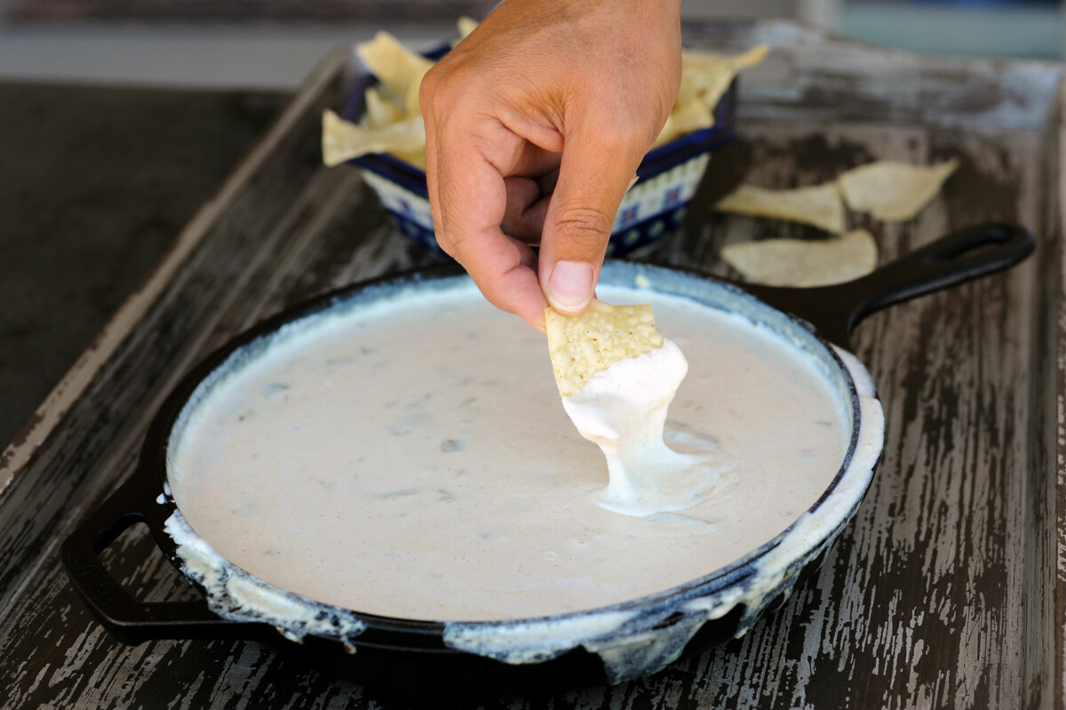 dipping chip into skillet of white queso dip.
