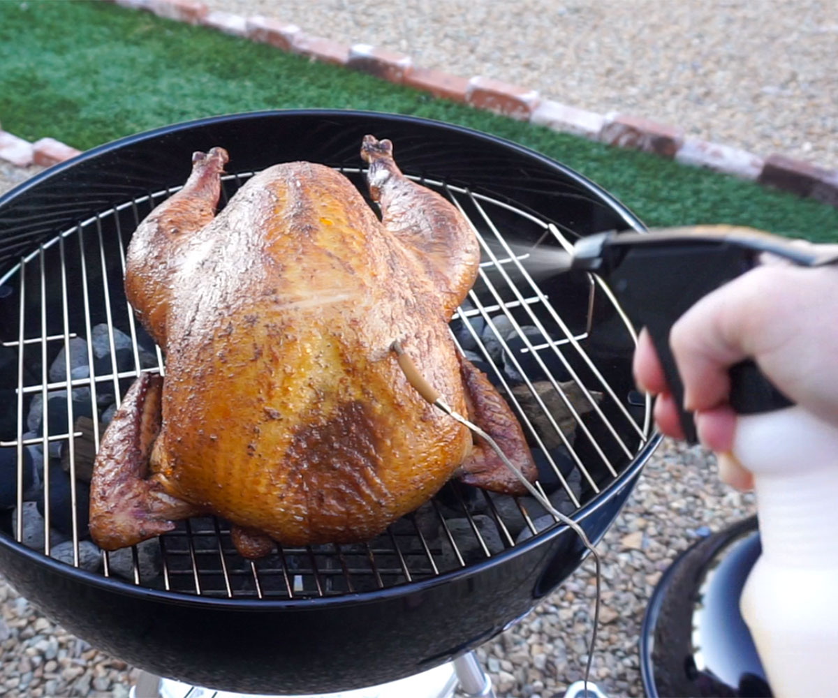 spritzing turkey on grill with apple cider.