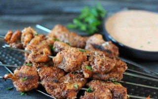 grilled alligator skewers on a gray background with side of sauce to top right