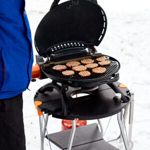Man grilling steaks on a portable BBQ, Snowy winter barbecue outdoors in the cold.