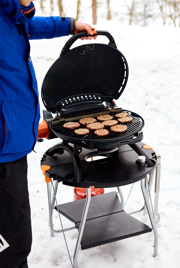 Man grilling steaks on a portable BBQ, Snowy winter barbecue outdoors in the cold.