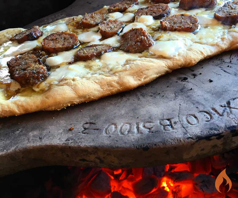 pizza topped with sausage on a ceramic plate over a fire
