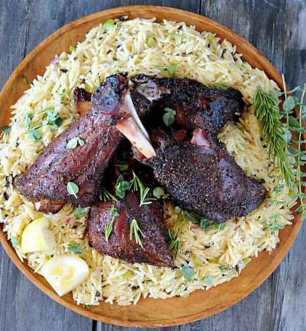 lamb shanks setting on a bed of orzo on a wooden round platter