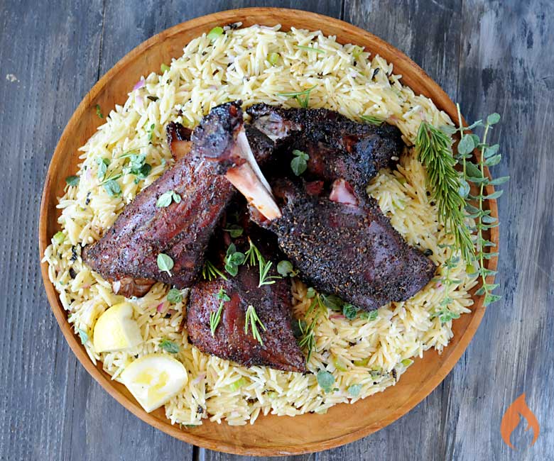 lamb shanks setting on a bed of orzo on a wooden round platter