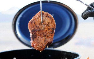 pork chop hanging from a hook above a black barrel grill