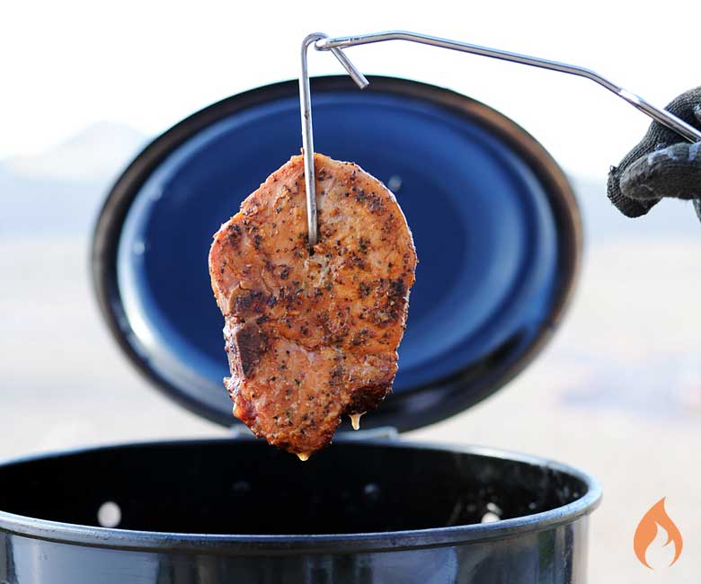 pork chop hanging from a hook above a black barrel grill