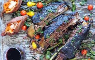 three smoked beef ribs with fresh vegetables on platter with red wine