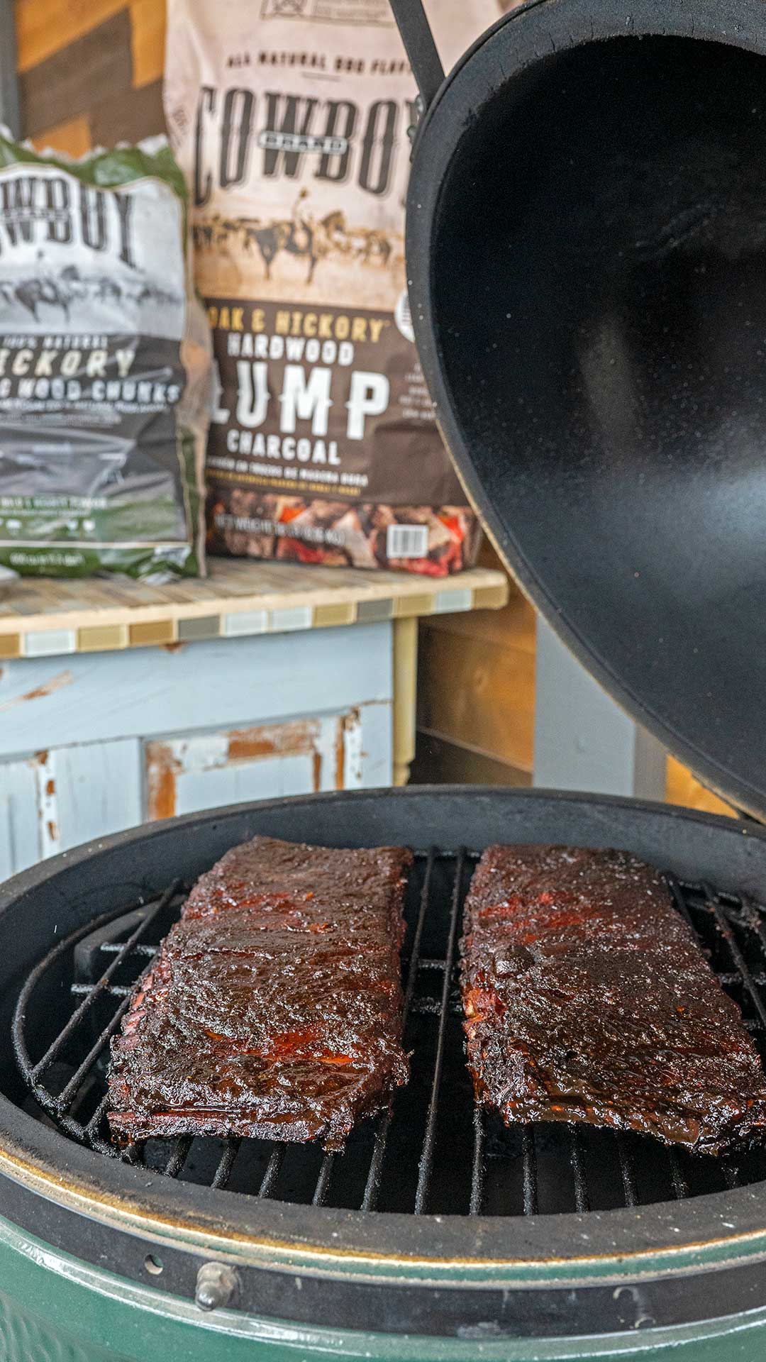 two racks of ribs on grill by bag of Cowboy lump charcoal and wood chunks