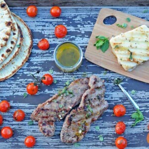 grilled New York Strip steak on a wooden platter with cheese, tomatoes and flatbread