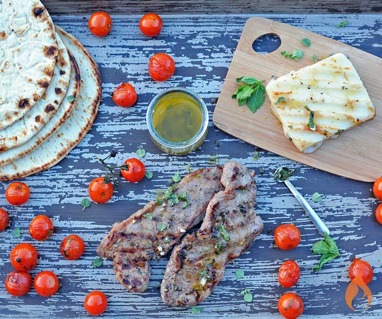 grilled New York Strip steak on a wooden platter with cheese, tomatoes and flatbread