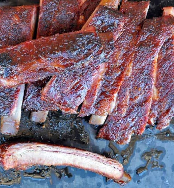sliced st louis style ribs on a black background with one rib at bottom