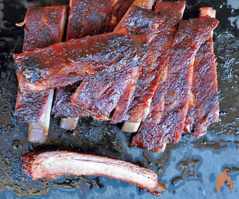 sliced st louis style ribs on a black background with one rib at bottom