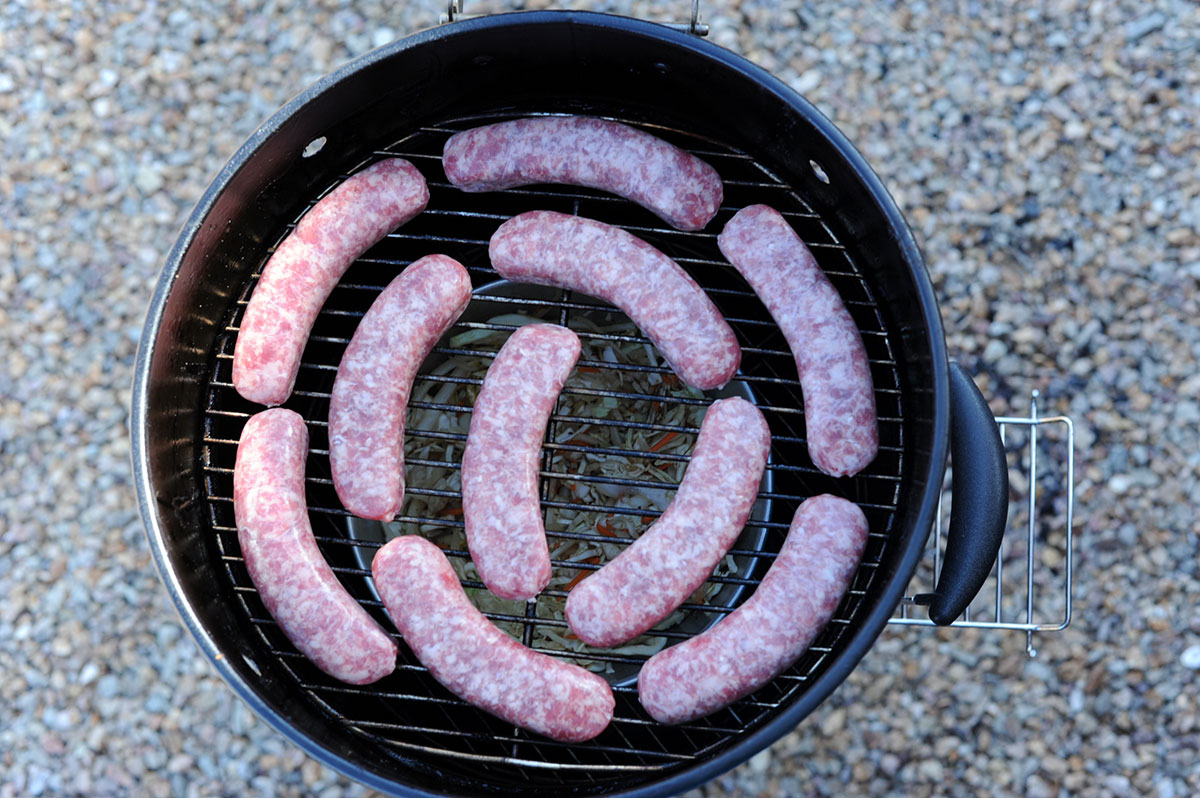 bratwursts on grill over bowl of cabbage.