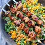skewers of grilled chicken atop lettuce and mango