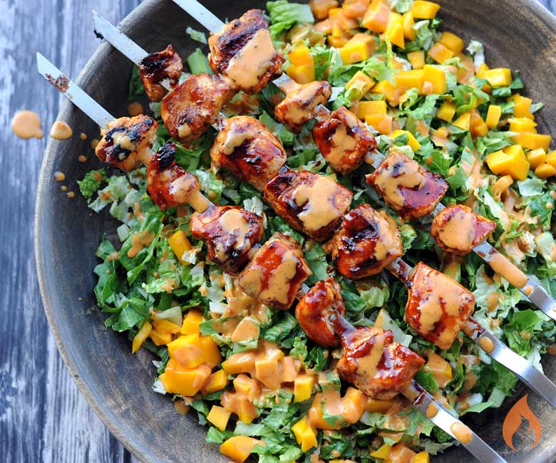 skewers of grilled chicken atop lettuce and mango