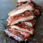 sliced sauced St. Louis Style ribs in a vertical row on black slate