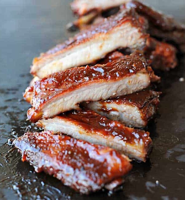 sliced sauced St. Louis Style ribs in a vertical row on black slate