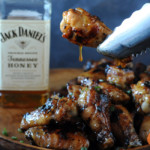 holding wing with tongs with glaze dripping off near bottle of Jack Daniels Honey
