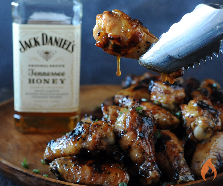 holding wing with tongs with glaze dripping off near bottle of Jack Daniels Honey