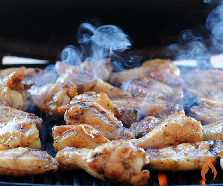 chicken wings cooking on a grill with smoke