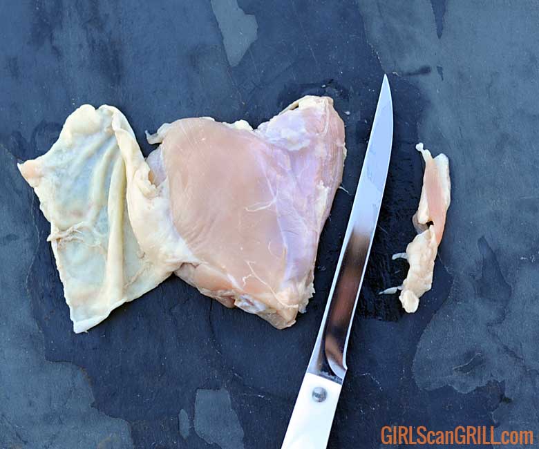 knife scraping off excess fat from raw chicken thigh
