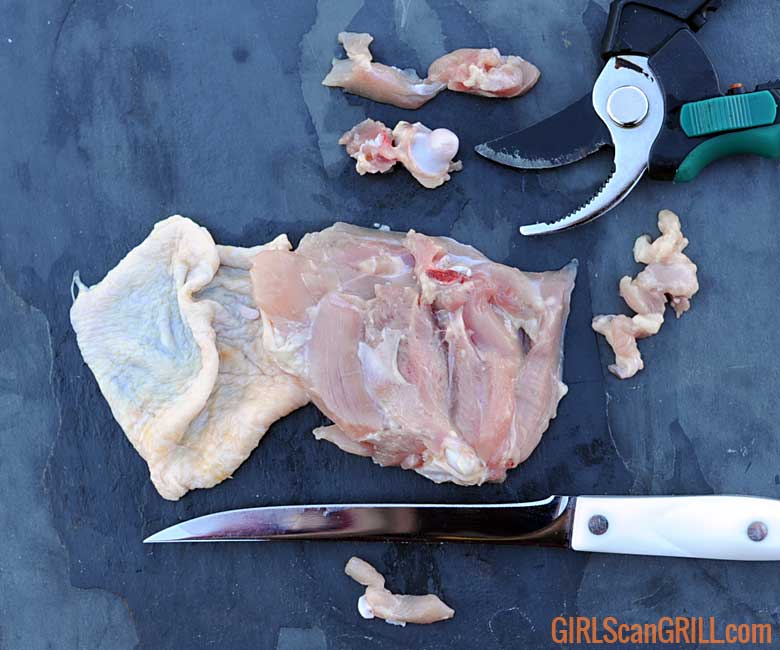 underside of chicken thigh with knife and shears and trimmed bone and fat