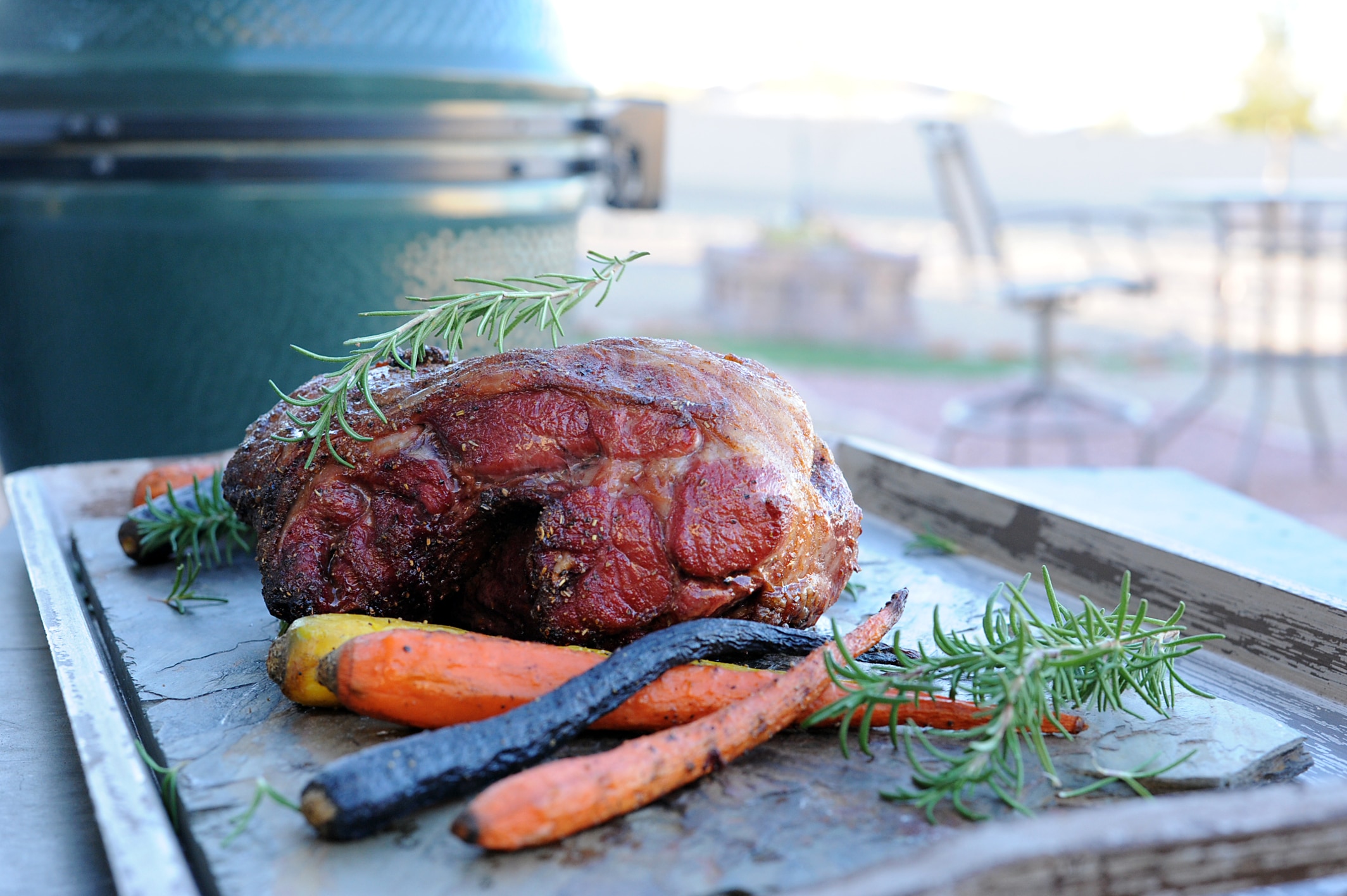 Roasted leg of lamb setting on table with carrots by grill