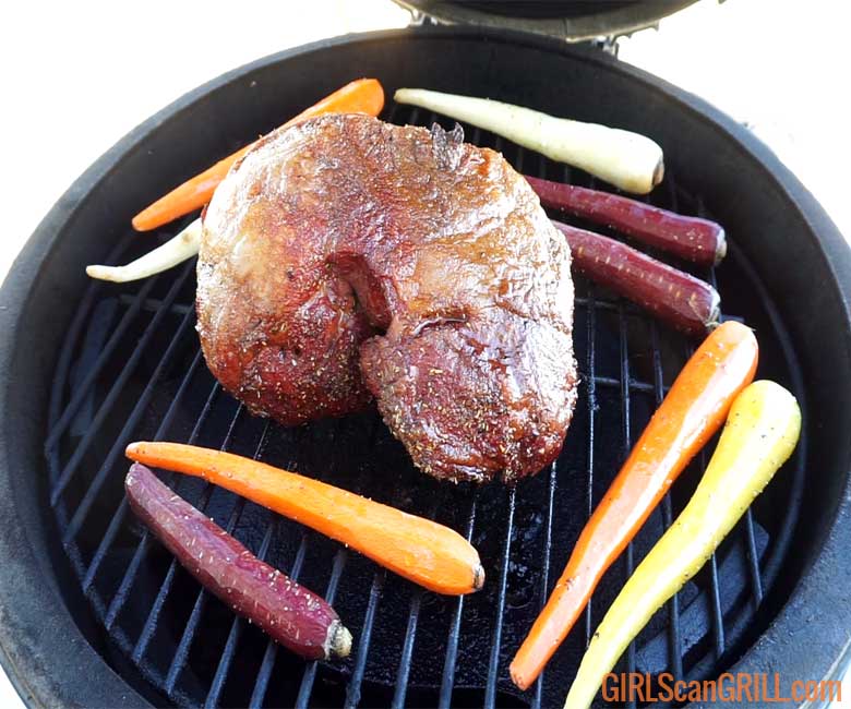 uncooked lamb roast setting on a black grill grate with carrots