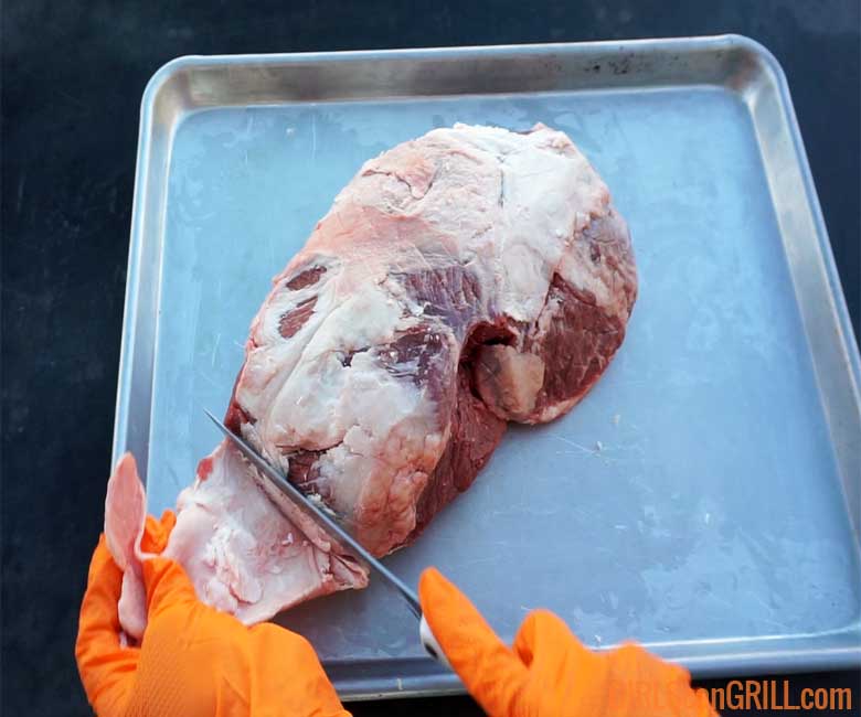 trimming lamb roast on pan while wearing orang gloves